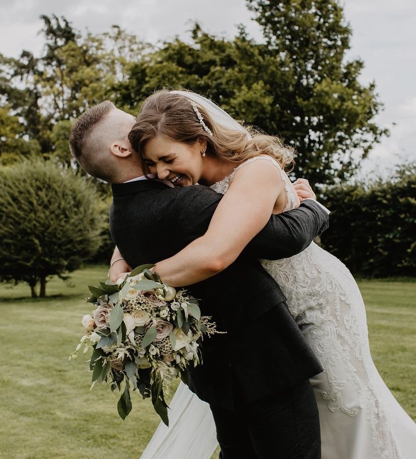 A bride holding a luxurious and overflowing wedding bouquet, custom-made by a Northern Ireland florist, hugging her husband